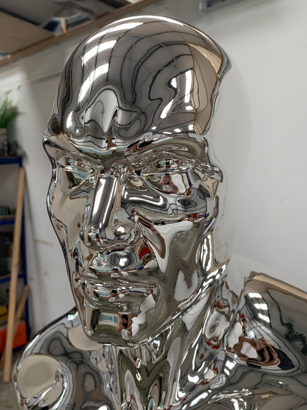 Highly polished mirrored chrome mannequin torso photographed in a fabrication workshop, highlighting the reflective finish and detailed facial features.