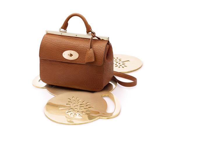 Studio product shot of a brown leather handbag presented on gold decorative display plates against a white background, suitable for retail and POS display imagery.