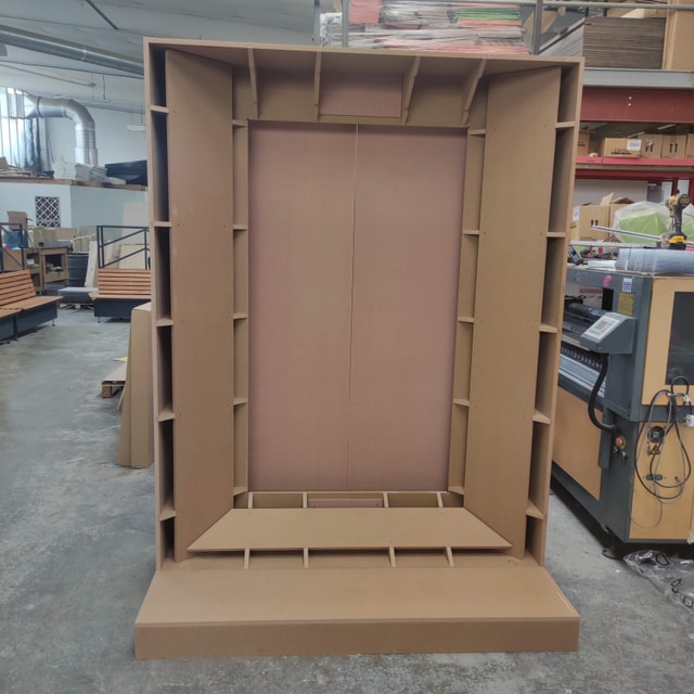 Unfinished MDF retail display fixture with shelving being fabricated in a workshop, shown next to a CNC/router machine.