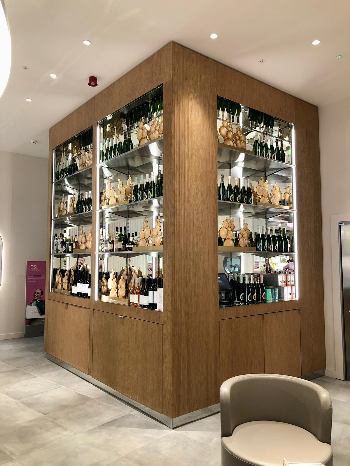 Premium in-store champagne display with illuminated mirrored shelving and wood cladding in a retail environment, ideal for merchandising and fixtures.