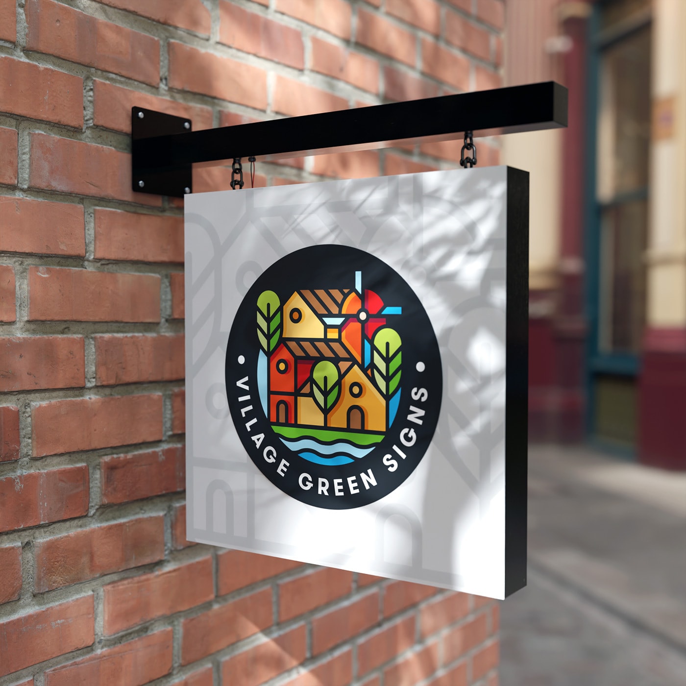 Wall-mounted projecting shop sign with a colourful circular 'Village Green Signs' logo on a white double-sided panel, hung from a black metal bracket on a brick exterior in a retail street setting.