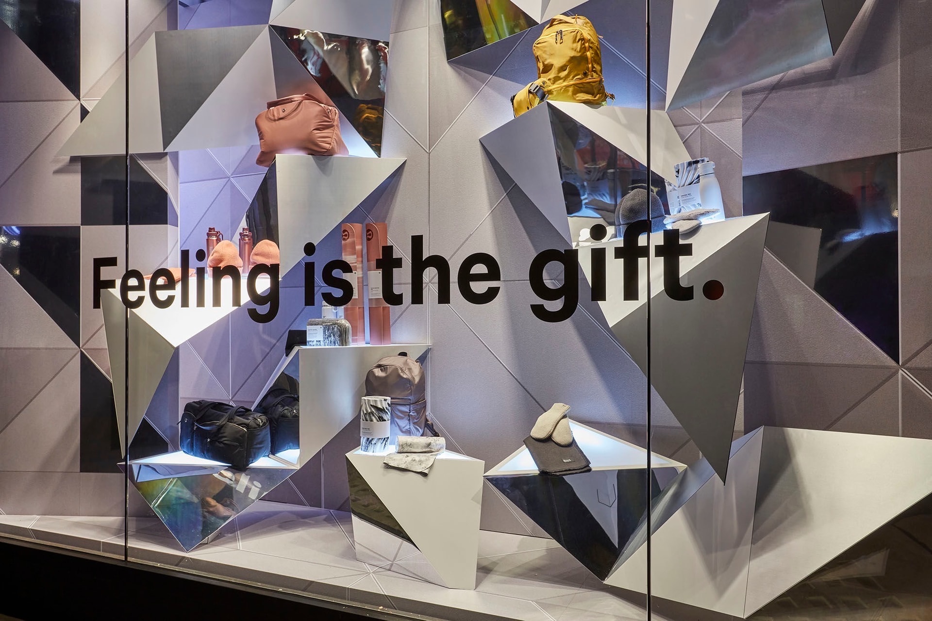 Retail storefront window with bold vinyl slogan and geometric mirrored display fixtures showcasing bags and accessories.